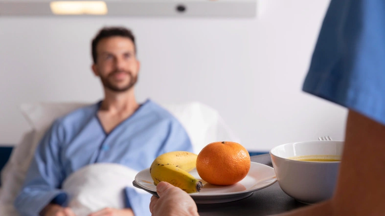 Profesional de salud entregando una bandeja con alimentos a un paciente hospitalizado que sonríe