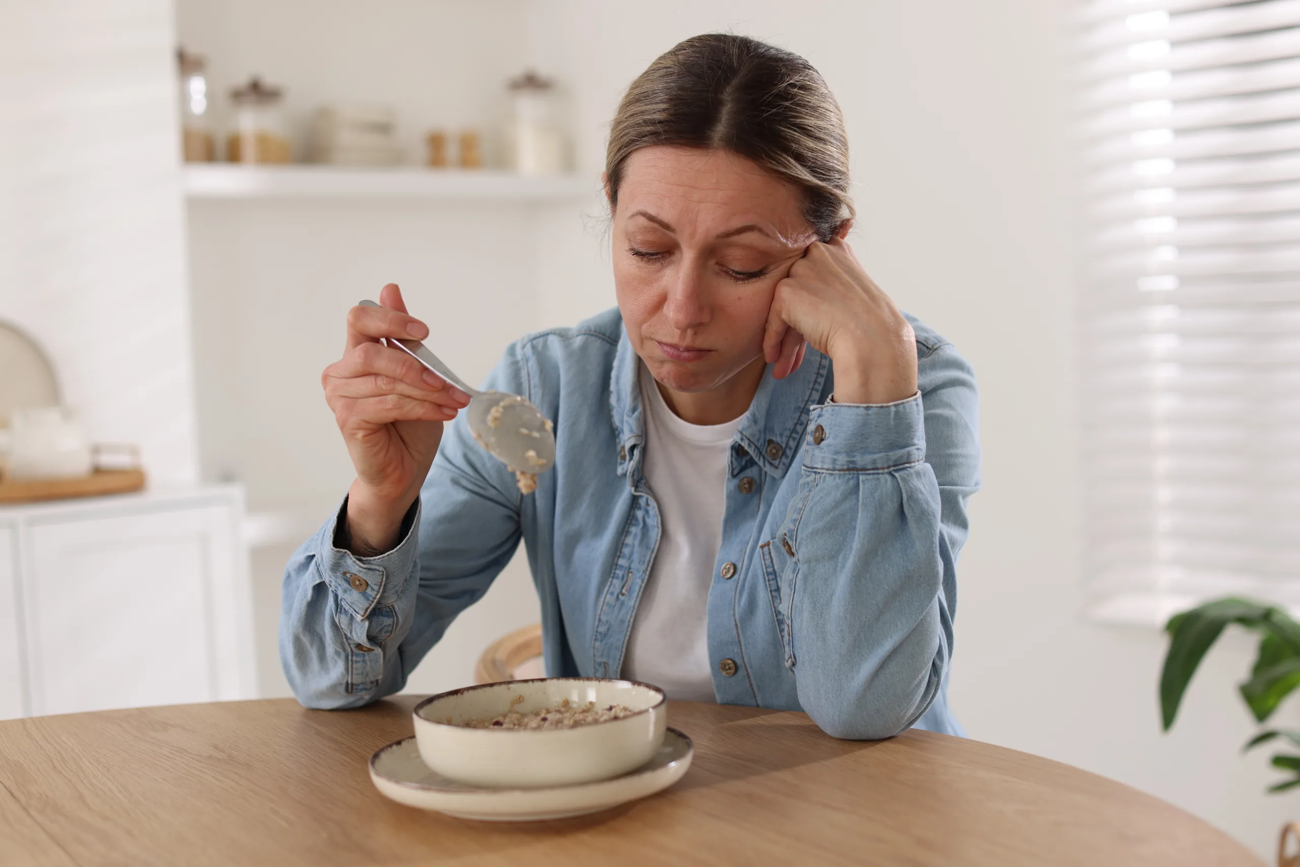 Mujer con expresión desanimada frente a un plato de avena, sin apetito.