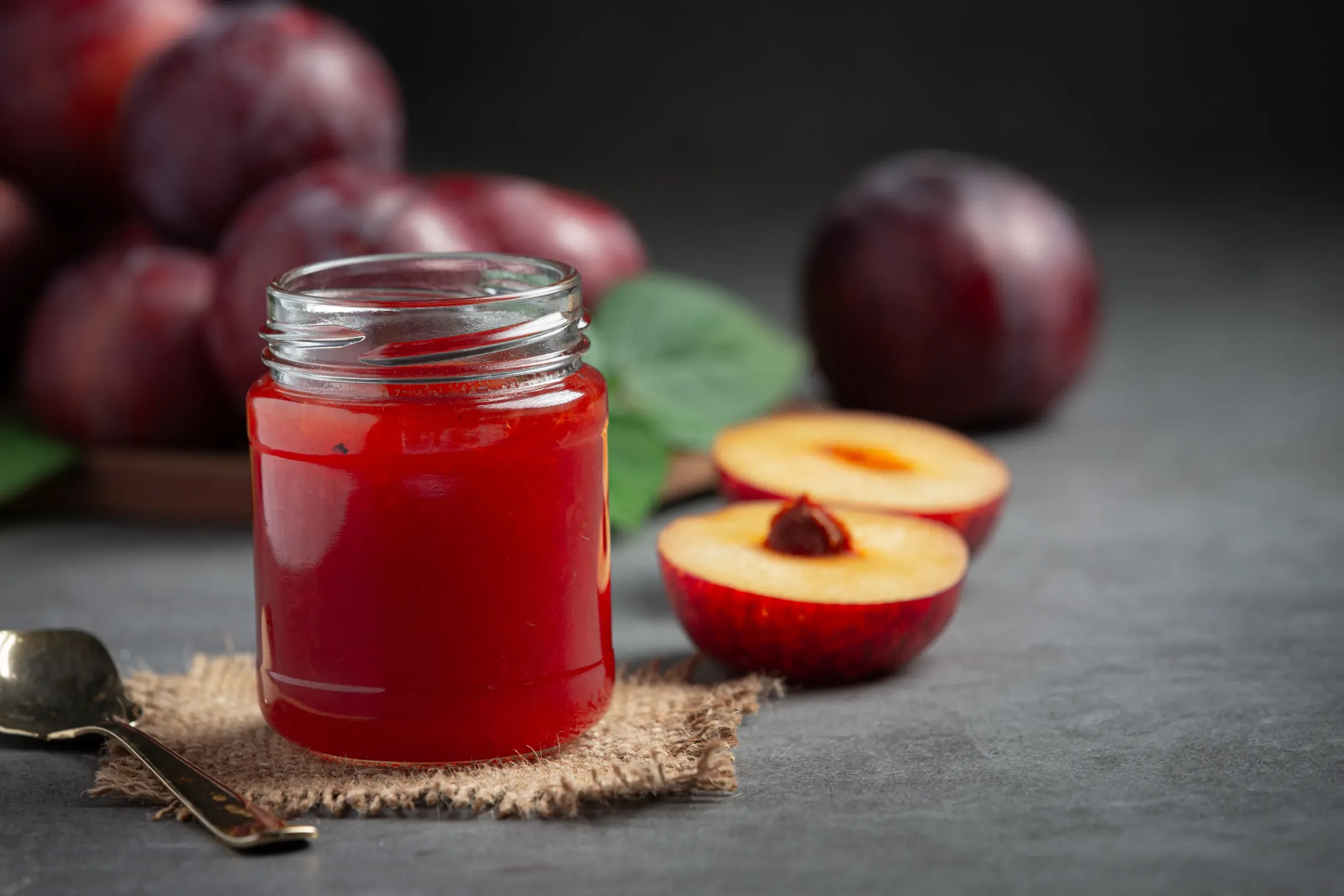 Frasco de mermelada de ciruela con frutas frescas y una cuchara al lado.
